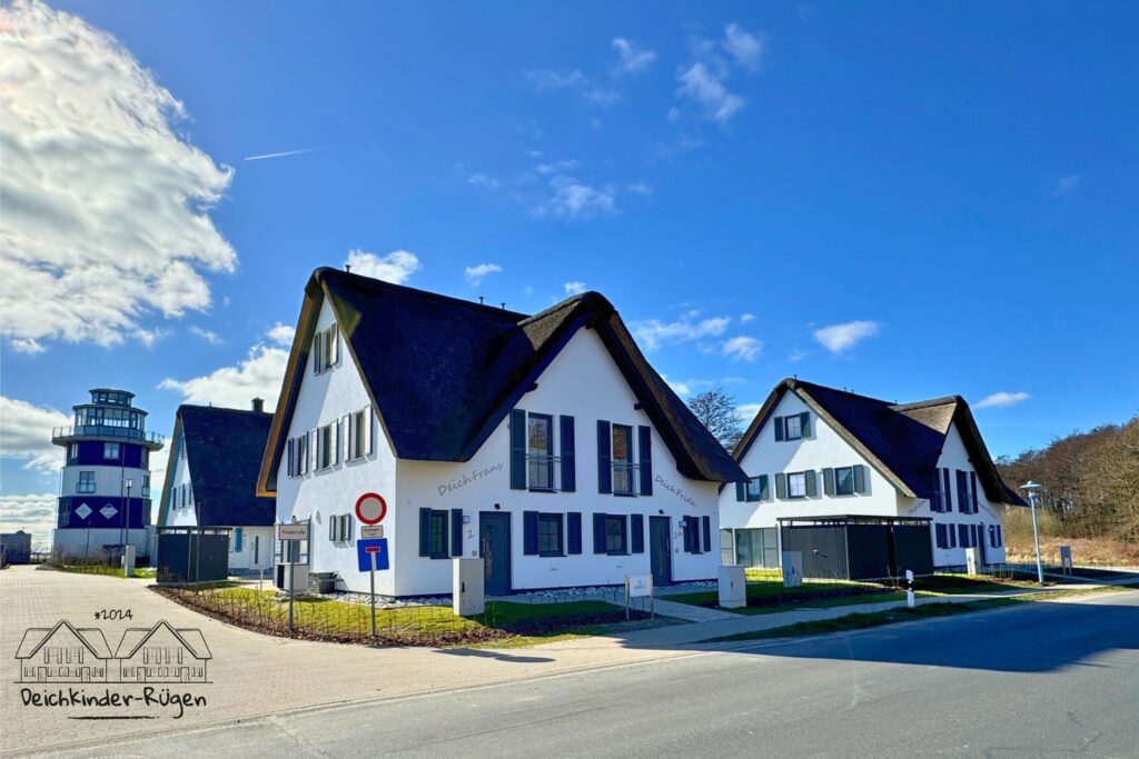 Drei moderne weiße Häuser mit Strohdächern neben einer Straße unter blauem Himmel.