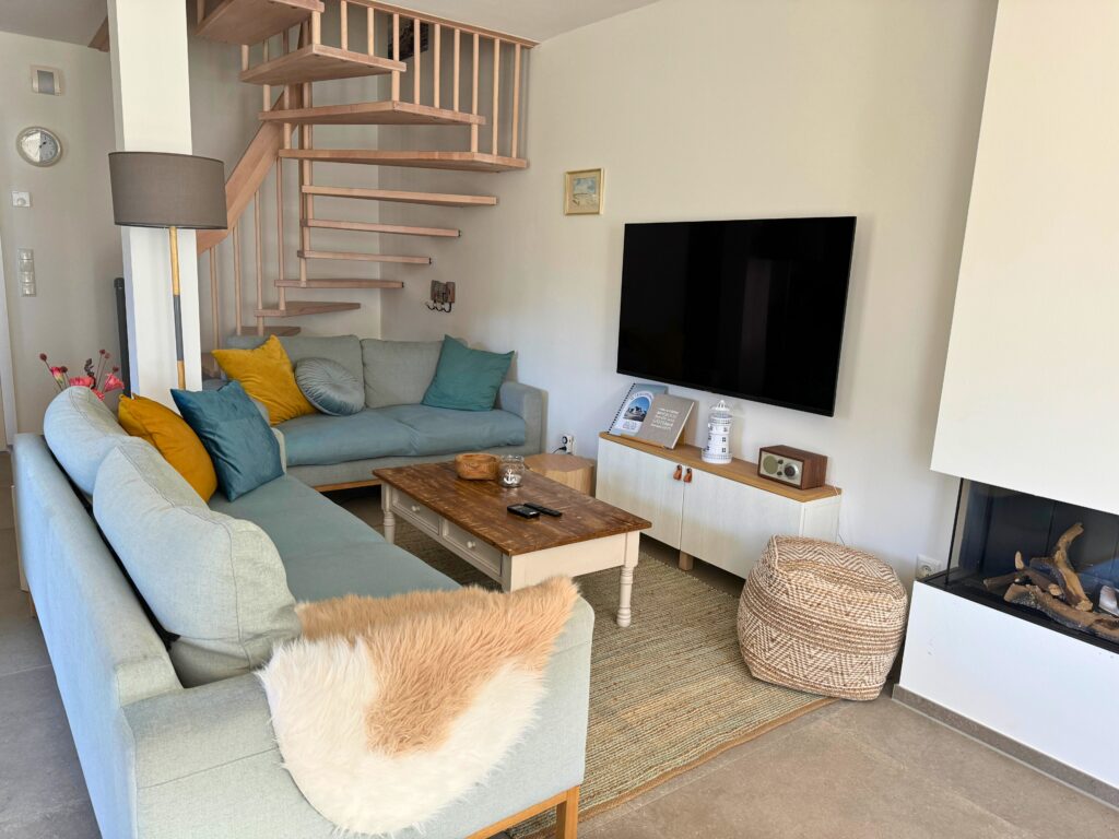 Modernes Wohnzimmer mit zwei Sofas, einem großen Fernseher und einer Holztreppe in der Ecke.
