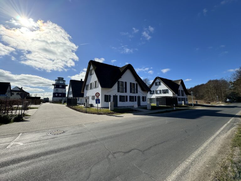 Weiße Häuser mit schwarzen Dächern und Fensterläden in der Nähe einer Straße unter einem blauen Himmel mit Wolken.