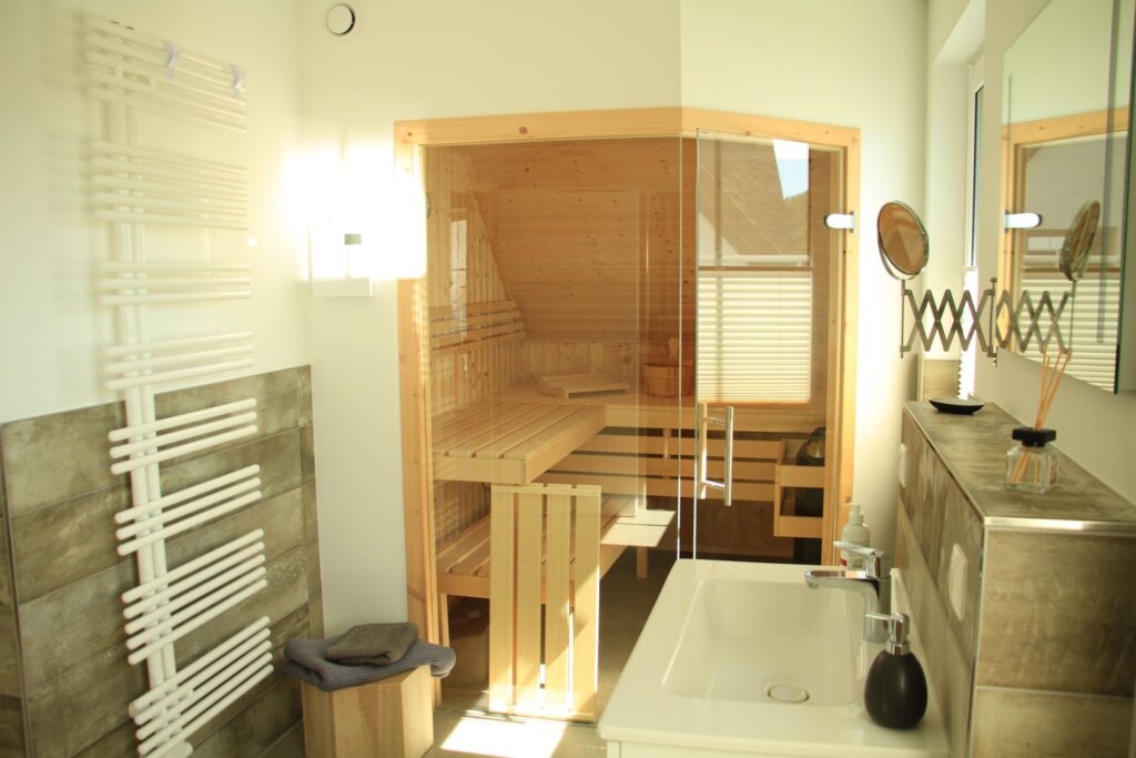 Modernes Badezimmer mit einer Holzsauna, Glastür, Waschbecken, Spiegel und Handtuchhalter.