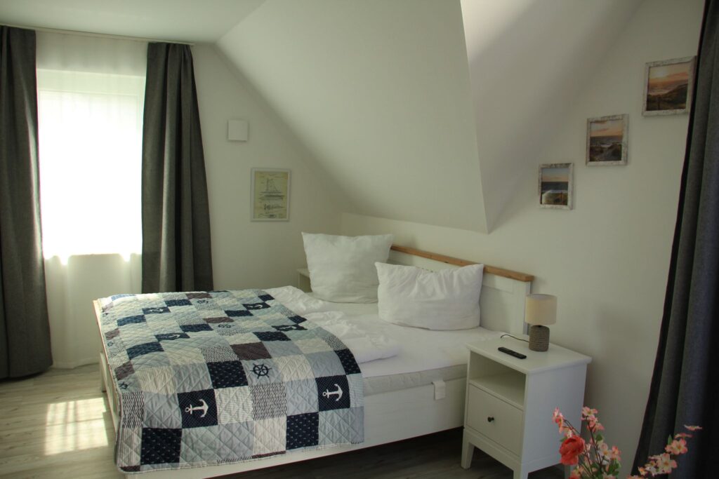 Schlafzimmer mit Doppelbett, Patchwork-Decke, Nachttisch und gerahmten Bildern an der Wand.
