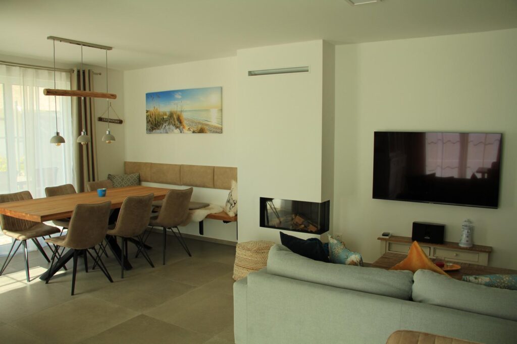 Moderner Wohn- und Essbereich mit einem an der Wand montierten TV, Kamin und großen Fenstern.